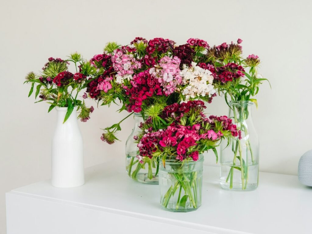 Ramos con flores rosas, granates y blancas en jarrones de vidrio sobre una mesa blanca